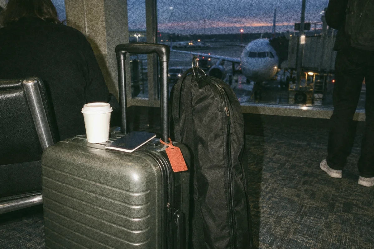 A sample suitcase and garment bag at an airport gate in the early light, an orange luggage tag