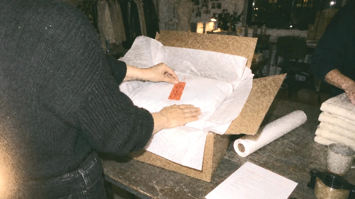 A garment wrapped in tissue in an open carton, an orange swing tag laid on top