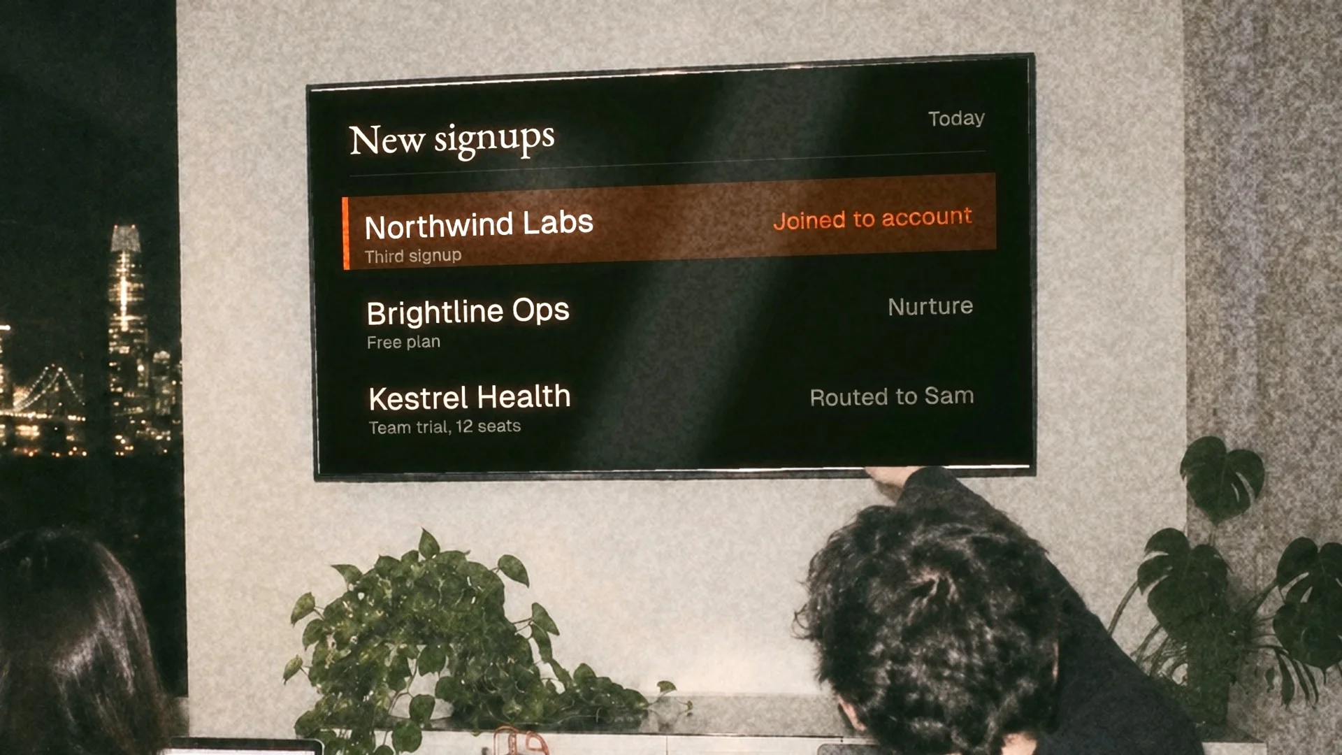 New signups arriving on a wall screen in an office at night, one highlighted in orange