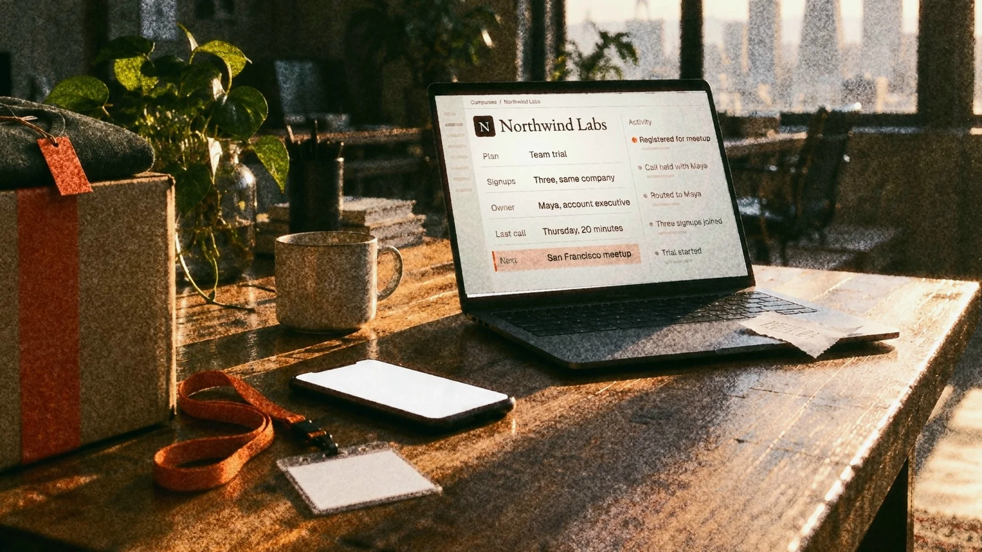 A laptop on a loft table at dawn showing an account record, a coffee cup beside it